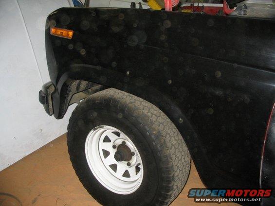 Close-up of a black SUV's front fender and wheel. The vehicle has a white rim and a knobby tire