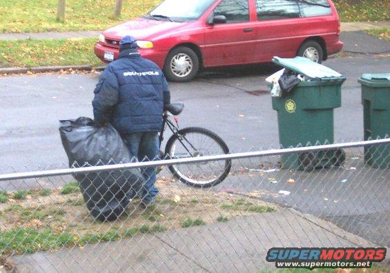 guy with garbage bag and bike next to trash cans, red van in background