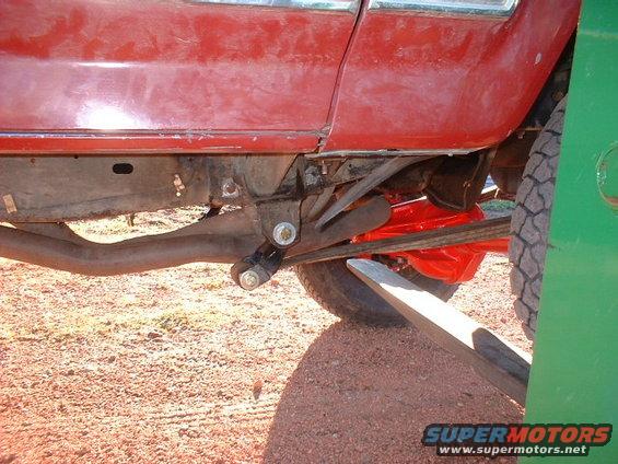 Close-up of a red truck's rear axle, leaf springs, and exhaust pipe. A green panel is on the right
