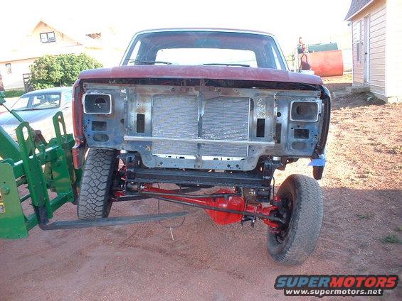 Red Ford F-250 truck front end with grille removed, being lifted by a green tractor. The radiator is visible
