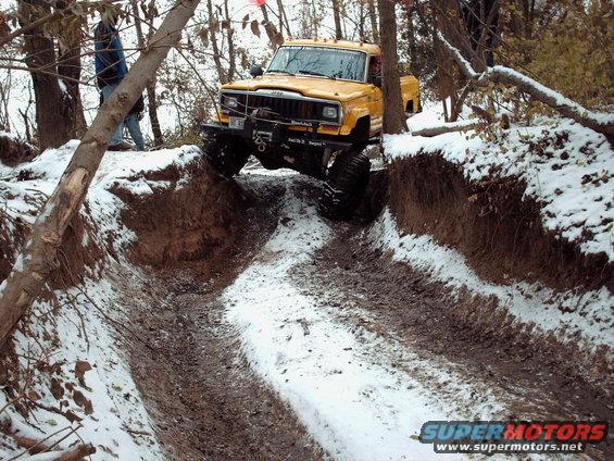 Yellow Jeep truck with large tires navigating a snowy ditch