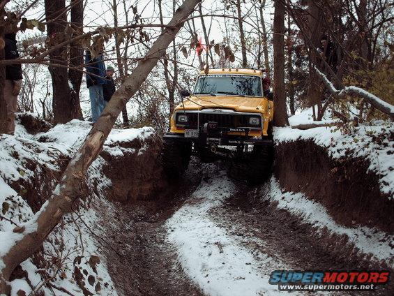 Yellow Jeep Cherokee with large tires navigating a snowy ditch off-road. License plate reads 'XL 8159'
