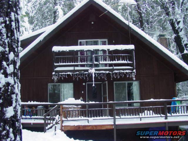wooden cabin covered in snow with icicles hanging from the roof and balcony