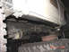 1990 Ford Bronco - The underside of a white 1990 Ford Bronco is visible, including its frame, suspension components, and a large tire.