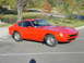 1978 Nissan 240SX - This red 1978 Nissan 240SX coupe is captured from a three-quarter front angle, with a scenic backdrop of water and trees.