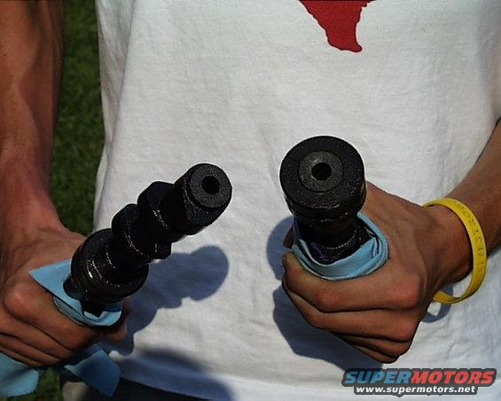 Two black camshafts held in hands, one with a blue cloth
