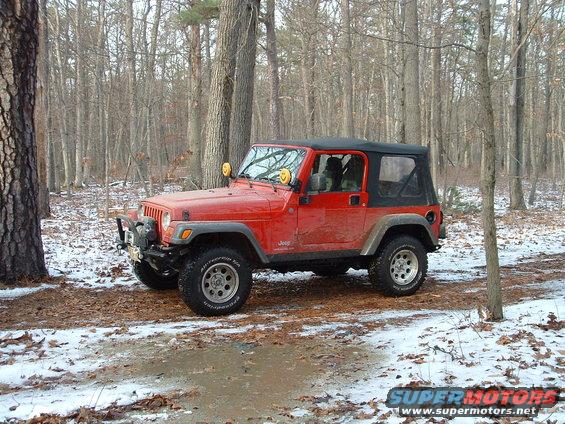 Red Jeep Wrangler with a soft top parked in a snowy wooded area