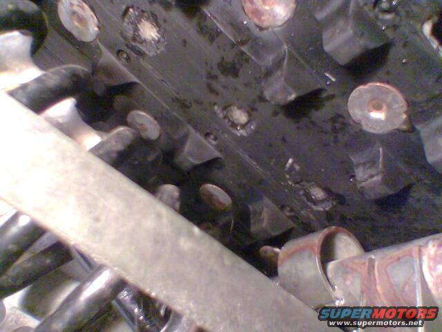 Close-up of a snowmobile track with visible lugs and fasteners. Some suspension components are also visible