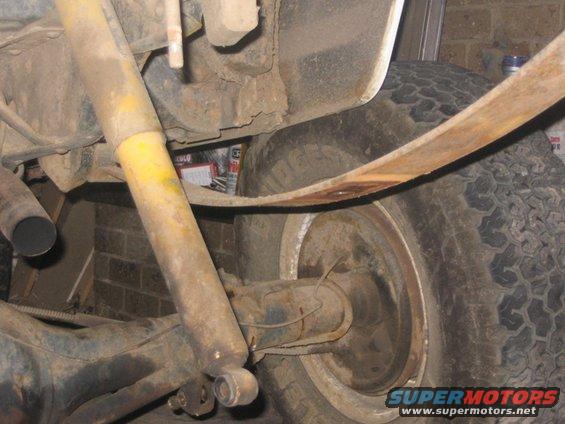 Close-up of a rusty leaf spring, shock absorber, and rear axle assembly