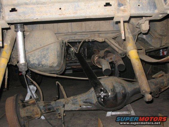 Underside of a vehicle showing the rear axle, differential, fuel tank, exhaust pipes, and shocks