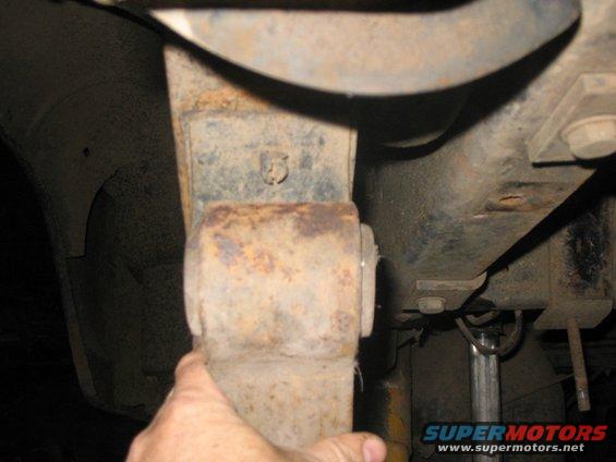 Rusty leaf spring assembly with a hand pointing to it, showing suspension parts