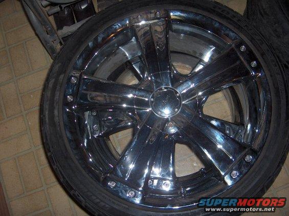 Chrome five-spoke wheel with a tire mounted. Part of a larger object is visible to the left