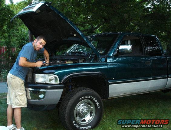 Green 1997 Dodge 2500 pickup truck with hood open, man working on engine, side view