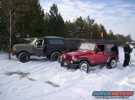 Red Jeep Wrangler and a dark SUV parked in the snow with trees in the background