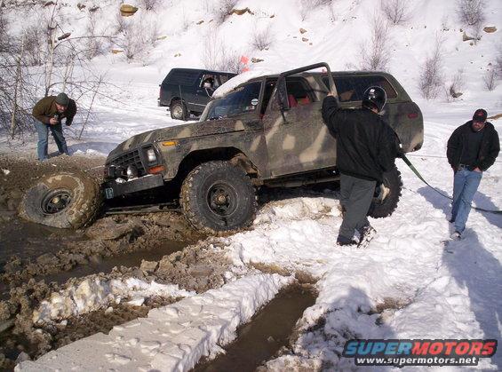 Camouflage SUV stuck in mud and snow, front wheel deep in mire