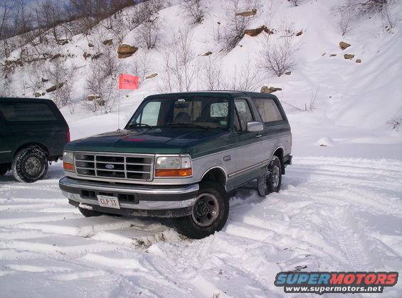 Green and silver Ford Bronco in snow, another dark SUV behind it