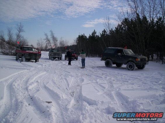Black Ford Bronco in snow with other vehicles and people around