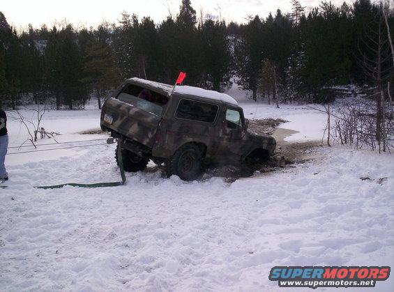 Camouflaged SUV stuck in mud and snow, being pulled by a strap