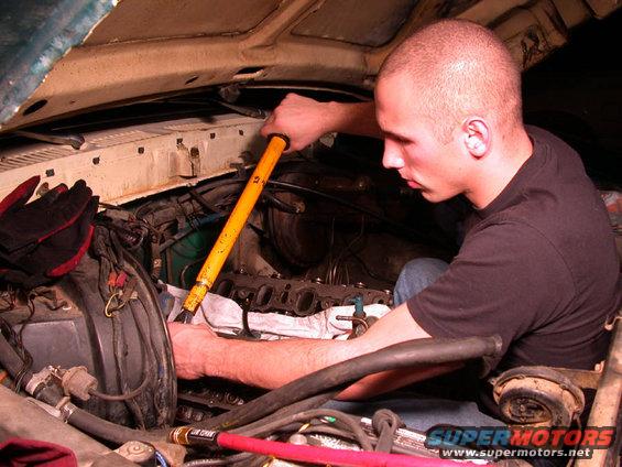 guy using a yellow tool to work on an engine, with gloves nearby