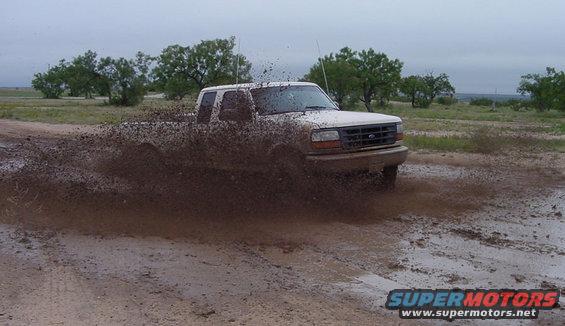 White pickup truck splashing mud while driving off-road. The grille suggests a 1995 model
