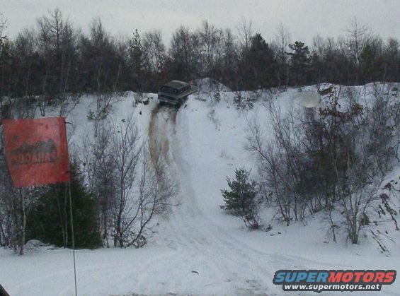 1996 Ford Bronco driving down a steep, snow-covered hill with trees in the background