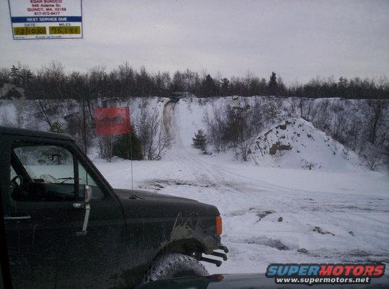 Dark off-road vehicle in snowy terrain with a dirt track going up a hill in the background