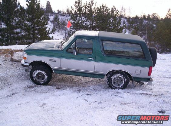 Green and silver Ford Bronco parked in snow. Bronco badge visible on the side