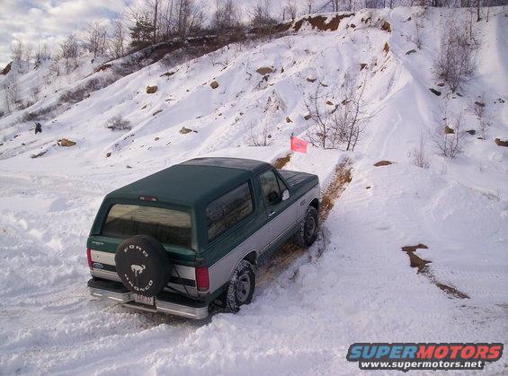 Green and silver Ford Bronco driving on a snowy hill. Spare tire on the back has a Bronco logo