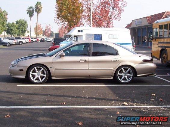 1998 Mercury Sable sedan, tan with black racing stripes on hood, parked in lot