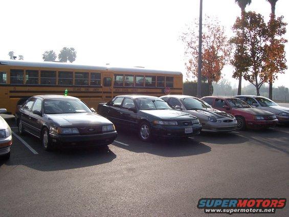 Dark 1998 Mercury Sable sedan parked in a lot with other cars and a school bus