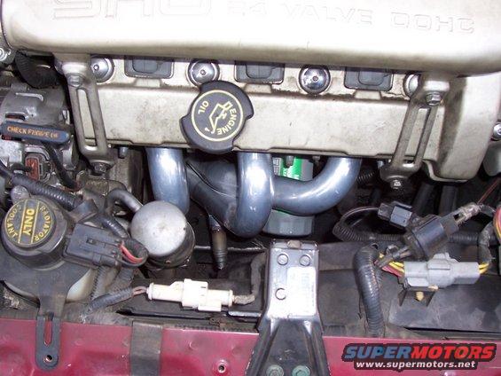 Engine bay close-up showing exhaust manifold, oil cap, and various hoses and connectors
