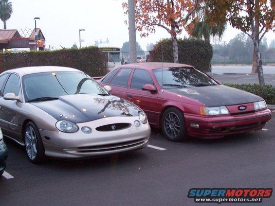Front view of a tan sedan with a black hood next to a red sedan with a black hood