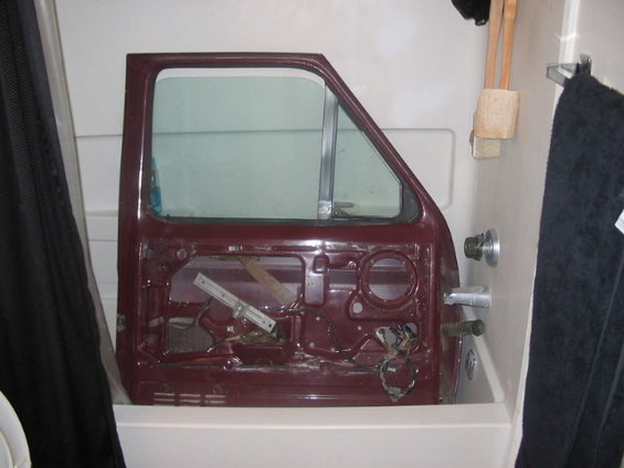 Maroon car door with window removed, showing interior mechanisms, resting in a bathtub