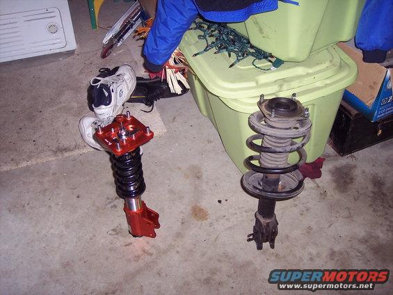 Two car suspension struts, one with an adjustable red top mount and black coilover, the other a standard strut assembly