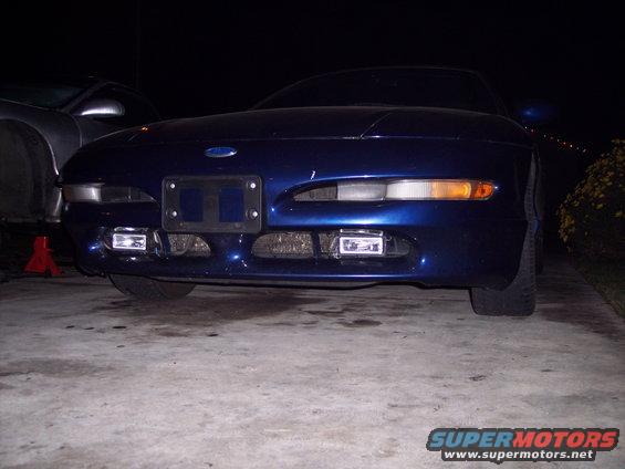 Front view of a blue 1995 Ford Probe parked on a concrete surface at night. Another car is partially visible to the left