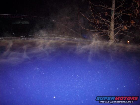 Blue car hood with steam rising off it at night