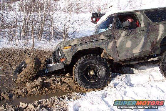 Camouflaged Ford Bronco stuck in mud and snow, another vehicle visible in background