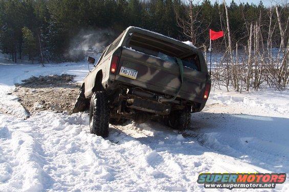 Rear view of a 1979 Ford Bronco stuck in snow, with a red flag on antenna