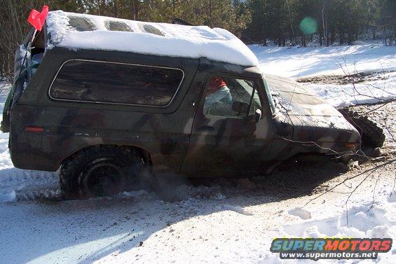 Camouflaged Ford Bronco stuck in snow and mud, with a red flag on top