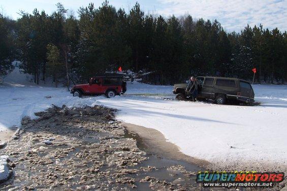 Red Jeep and green SUV stuck in snow and ice, with trees in background