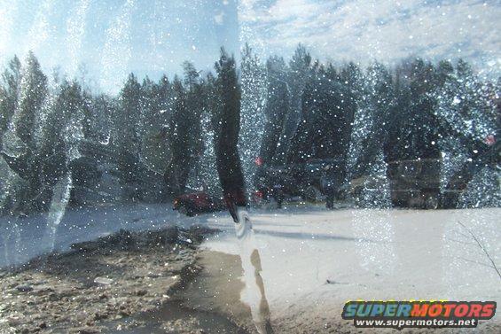 Red SUV partially visible through a snow-covered windshield with trees and other vehicles in the background