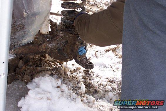 close-up of a dirty vehicle suspension component with a coil spring, being worked on in snowy conditions