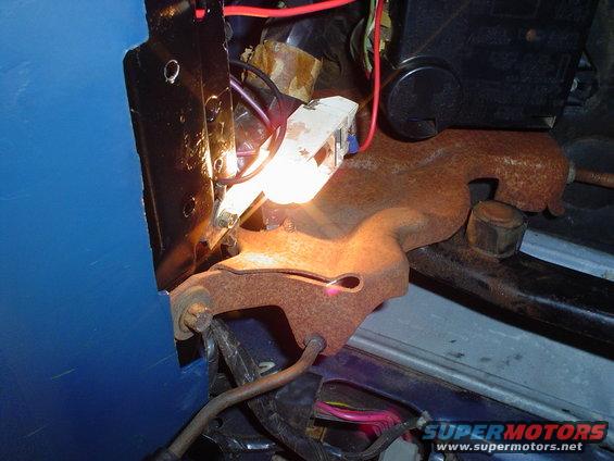Close-up of a rusty metal bracket with a light bulb and electrical wiring, showing blue interior paneling