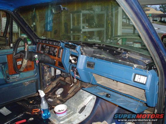 Interior of a blue truck with dashboard removed, showing wiring and components. Steering wheel and driver's side door panel visible
