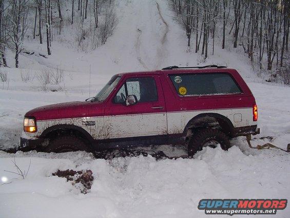 Red and white 1994 Ford Bronco stuck in deep snow, front right wheel submerged