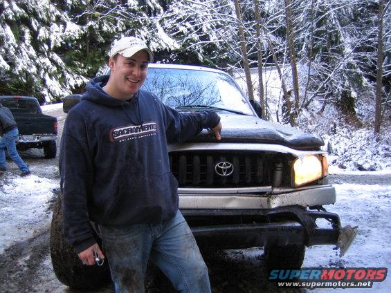 Front view of a Toyota Tacoma with a man standing next to it in a snowy environment
