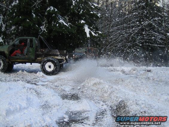 Two off-road trucks driving through snow and slush, kicking up water