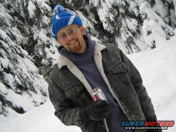Man in blue hat and denim jacket holding a can in snowy woods