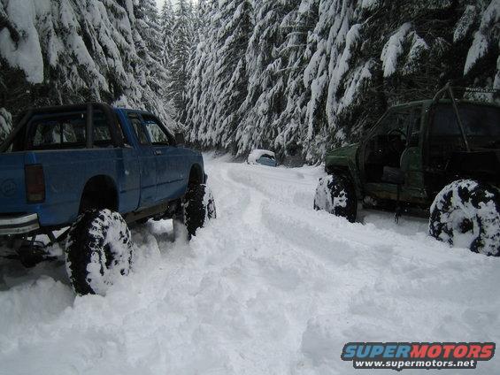 Blue pickup truck and green off-road vehicle in deep snow on a wooded road
