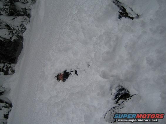 Person partially buried in snow, with boots visible. A rock face is to the left